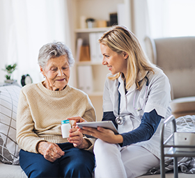 A caregiver and an older woman sitting together on a sofa, sharing a cup of tea and a conversation.